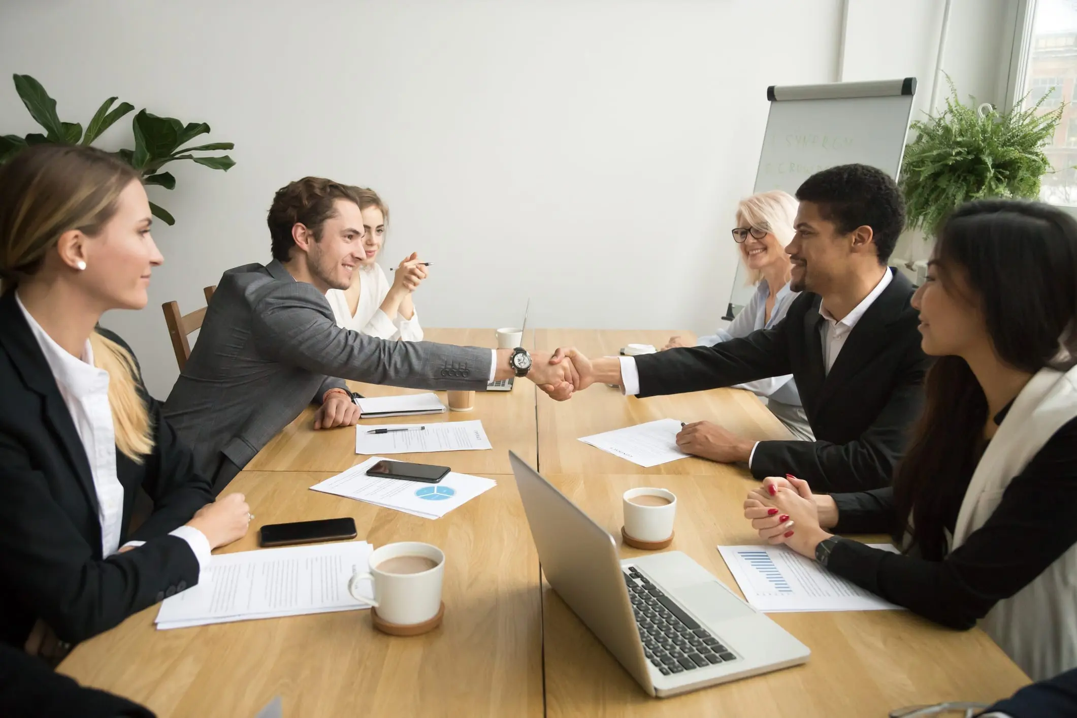 Diverse businessmen shaking hands after signing contracts at group meeting